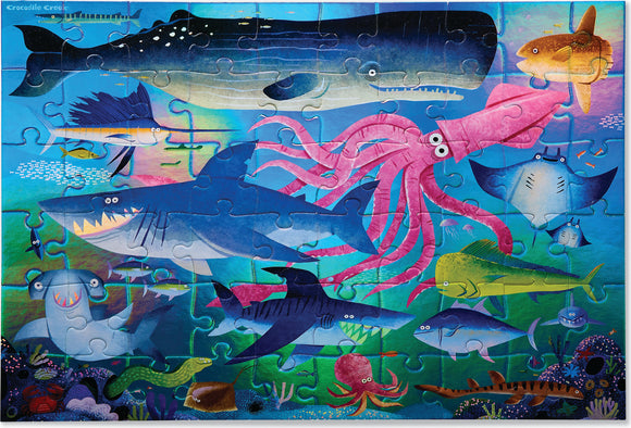 A colorful jigsaw puzzle featuring a vibrant underwater scene with various sea creatures including sharks, an octopus, and a whale, designed by Crocodile Creek. This 60-piece puzzle showcases bright colors and playful illustrations, making it perfect for both kids and families.