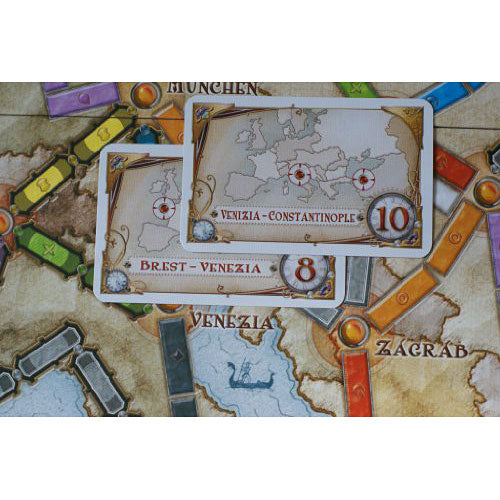 Close-up of Ticket to Ride: Europe game cards showing routes between Venizia and Constantinople, and Brest and Venizia, laid out on a colorful game board. The vibrant design features various city names and track colors.