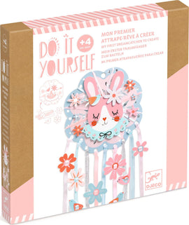 The 'Dreamer Dreamcatcher' DIY kit by DJECO features a colorful design with a cute bunny face, vibrant flowers, and attached ribbons. Ideal for children aged 4 and above to create their own decorative dreamcatcher.