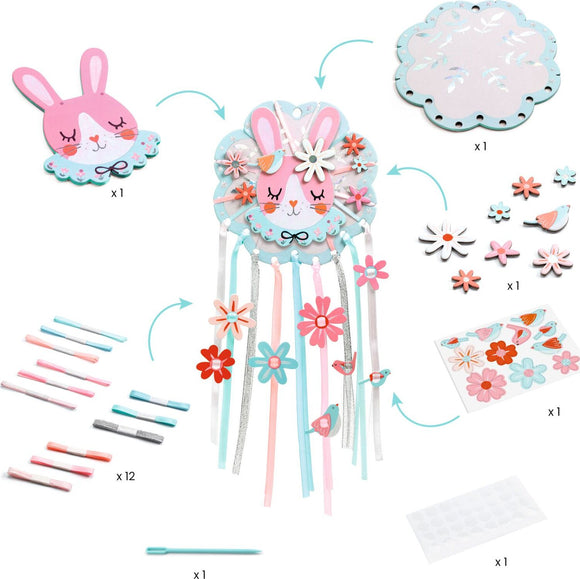 A DIY kit titled Dreamer Dreamcatcher by DJECO, featuring colorful components including a bunny head centerpiece, decorative flowers, ribbons, and crafting tools. The image showcases the various parts needed to create a charming dreamcatcher designed for children to engage in imaginative play and develop crafting skills.
