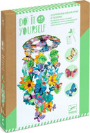 A colorful DIY kit for creating a springtime decorative mobile, featuring various vibrant flowers, butterflies, and leaves. The kit includes pieces for painting and assembling a cheerful hanging decoration. Features a green-themed box design with illustrations and instructions.