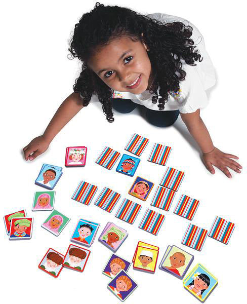 A joyful child sits on the floor playing the 'I Never Forget a Face' Matching Game by Eeboo. Colorful cards featuring diverse facial illustrations are scattered around. The child is smiling and engaging with the game, showcasing a fun and interactive way to enhance memory and recognition skills.