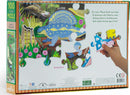 Eeboo's 'Land of the Dinosaurs' jigsaw puzzle featuring vibrant dinosaur illustrations and a hand holding a puzzle piece. Back of the box highlights a colorful prehistoric landscape with flowers and trees, showcasing puzzle pieces in actual size.