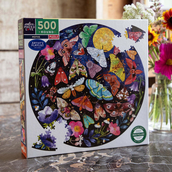 Eeboo Pebbles jigsaw puzzle featuring a vibrant design of moths and flowers in a circular arrangement on the box. The puzzle comprises 500 round pieces and is made from recycled materials. The packaging highlights an 'Artist's Playlist' included for a unique experience.