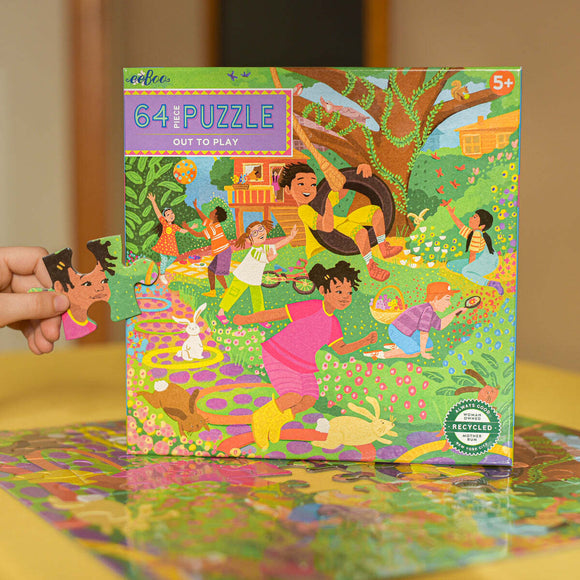 Eeboo's 'Out to Play' 64-piece jigsaw puzzle features vibrant illustrations of children playing outdoors in a colorful garden setting, surrounded by flowers, animals, and playful activities. A child is holding one piece of the puzzle, emphasizing interactivity and fun. Ideal for ages 5 and up.