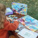 A child is assembling the 100-piece 'Love of Sharks' jigsaw puzzle by Eeboo on a wooden table. The puzzle showcases colorful illustrations of various shark species amidst a vibrant underwater scene. The puzzle box is visible, and a cloth bag labeled 'Good Green Bag' is also on the table.
