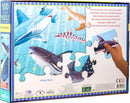 The 'Love of Sharks' jigsaw puzzle by Eeboo features a colorful illustration of various species of sharks swimming in a vibrant underwater scene. The packaging showcases a hand holding a puzzle piece, demonstrating the playful and educational theme. The puzzle consists of 100 pieces, ideal for children and adults alike who are fascinated by marine life.