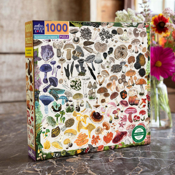 The Mushroom Rainbow jigsaw puzzle by Eeboo features a colorful assortment of 1000 different mushroom illustrations, showcasing various shapes, sizes, and colors. The puzzle box design includes detailed images of fungi along with text labels, set against a neutral background. The packaging highlights that it is made from recycled materials, making it an eco-friendly choice for puzzle enthusiasts.