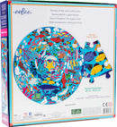 The Under the Sea Round Puzzle by Eeboo features an underwater scene brimming with colorful marine life including fish, jellyfish, and a giant whale. The puzzle is presented in a circular format with a diameter of 20 inches, showcasing vibrant illustrations that invite exploration and creativity. It comes in a box with a preview of the puzzle design and an actual piece displayed next to it.