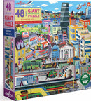 Eeboo's 'Within the City' jigsaw puzzle features a vibrant, illustrated cityscape with various buildings, vehicles, and people engaging in different activities. The box displays the title, piece count (48), and an informational poster included.