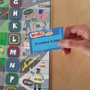 A hand holds a blue 'Word On The Street' game card that reads 'A country in Asia'. The game board features colorful graphics, including street signs, characters, and vehicles, set against a city backdrop.