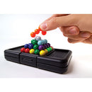 A hand is placing a colorful round plastic piece onto a stack of similar pieces in a black mechanical puzzle. The puzzle features a series of colorful marbles arranged in a pyramid, showcasing vibrant colors like red, blue, green, yellow, and purple. The base of the puzzle has a compact design with a storage compartment, emphasizing its portable and engaging nature for problem-solving activities.