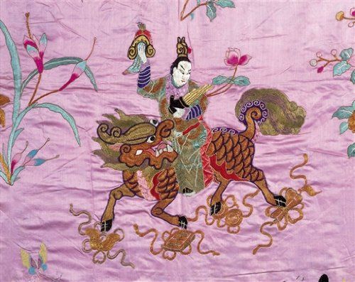 A vibrant jigsaw puzzle featuring an intricate depiction of a Chinese god riding a mythical creature adorned with embroidery. The background is soft pink, accentuated by floral motifs and swirling patterns, enhancing the artwork's cultural significance.