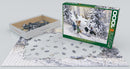 Eurographics jigsaw puzzle titled 'It's Your Turn' by Douglas R. Laird. The puzzle features a snowy scene with children playing in winter attire, surrounded by trees. The box is shown alongside scattered pieces on a flat surface, highlighting the 1000-piece count and intricate details of the artwork.