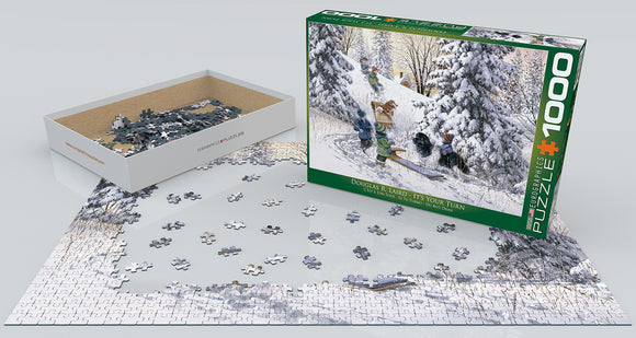 Eurographics jigsaw puzzle titled 'It's Your Turn' by Douglas R. Laird. The puzzle features a snowy scene with children playing in winter attire, surrounded by trees. The box is shown alongside scattered pieces on a flat surface, highlighting the 1000-piece count and intricate details of the artwork.