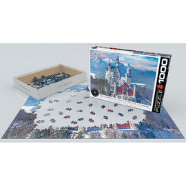 A 1000-piece jigsaw puzzle titled 'Neuschwanstein Castle in Winter' by Eurographics. The image features a snowy scene of the iconic Neuschwanstein Castle surrounded by snow-covered mountains. The puzzle pieces are scattered on the table, with the box displayed next to it, showcasing the beautiful artwork on the front.