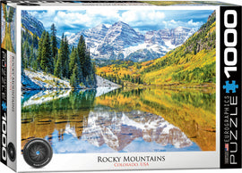 Eurographics Rocky Mountain National Park jigsaw puzzle featuring a stunning landscape scene of the Rocky Mountains in Colorado. The image displays tall pine trees, a serene lake reflecting the surrounding mountains, and vibrant autumn foliage.
