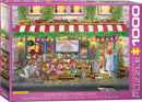 Plush Petals Florist jigsaw puzzle by Eurographics featuring a charming flower shop scene. A young woman in a sun hat stands admiring the vibrant floral display outside, surrounded by colorful flowers and plants. The flower shop has a quaint facade with a striped awning and cozy lights, exuding a delightful atmosphere of springtime blooms.