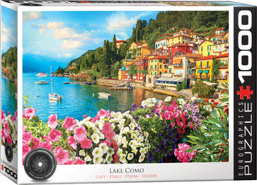 A colorful jigsaw puzzle box featuring a picturesque scene of Lake Como in Italy, showcasing vibrant houses along the lakeside, lush greenery, and blooming flowers in the foreground. The puzzle contains 1000 pieces and is created by Eurographics, highlighting the natural beauty of the Italian landscape.