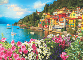 A vibrant jigsaw puzzle featuring a picturesque view of Lake Como, Italy. The scene showcases colorful buildings along the shoreline, lush greenery, and beautiful flowers in the foreground with boats gently floating on the bright blue water under a clear sky.