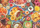 A vibrant jigsaw puzzle featuring a beautifully arranged breakfast table, showcasing an array of colorful dishes including fresh fruits like oranges, bananas, and kiwis, pastries like croissants and donuts, creamy yogurt, and cups of coffee. The setting highlights indulgent breakfast favorites, with a wooden tabletop enhancing the inviting atmosphere.