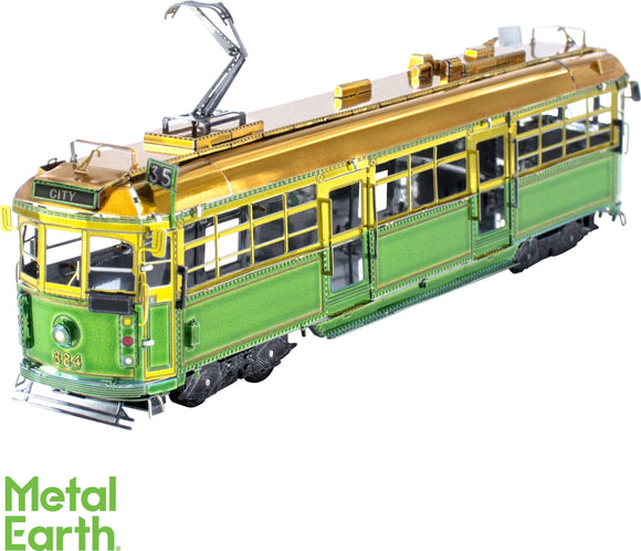 A detailed model of the Melbourne W-Class tram made from metal by Fascinations. It features a vibrant green and gold color scheme and intricate detailing, showcasing its realistic design. The tram is positioned at an angle, highlighting its showcase of craftsmanship with visible windows, wheels, and overhead power lines.