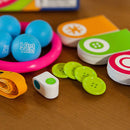 A colorful game set by Fat Brain Toys titled 'I Got This'. The image features vibrant blue balls embossed with the phrase 'I Got This', a pink ring, green buttons, and a white dice-like object. The game also includes various colorful cards with shapes and symbols, all arranged on a wooden surface, showcasing a fun and engaging interactive experience.