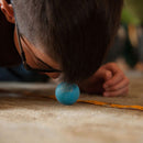 A child with glasses is laying on the floor, intently focused on a blue ball with 'I Got This!' printed on it, as they move it along a measuring tape on the carpet. This engaging game encourages hand-eye coordination and concentration.