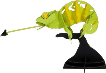 A vibrant 3D paper model of a chameleon crafted from colorful cardstock. The chameleon has a green body with distinctive yellow accents and is posed on a black base, showcasing its long tongue reaching out towards a small, black insect. This DIY kit allows for creative assembly and display.