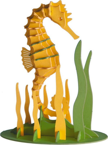A colorful 3D paper model of a seahorse, crafted from layered yellow and green paper. The seahorse stands upright amidst green paper seaweeds, showcasing intricate details and a playful design suitable for DIY enthusiasts.