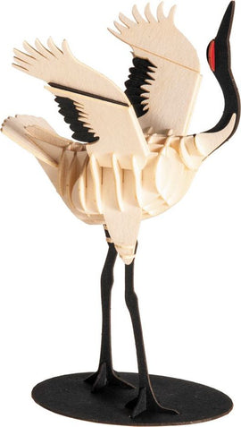 A detailed 3D paper model of a Whooping Crane made from layered wood. The crane features intricately designed wings spread wide and a slender neck, standing on a black base. The model highlights the graceful posture and distinctive features of the bird, including its red eye and unique feather patterns.