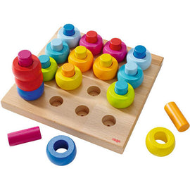 Pegging Game Rainbow Whirls by Haba, featuring a colorful set of wooden pegs in various shapes and sizes arranged on a wooden board. The game promotes fine motor skills and color recognition, making it ideal for young children.