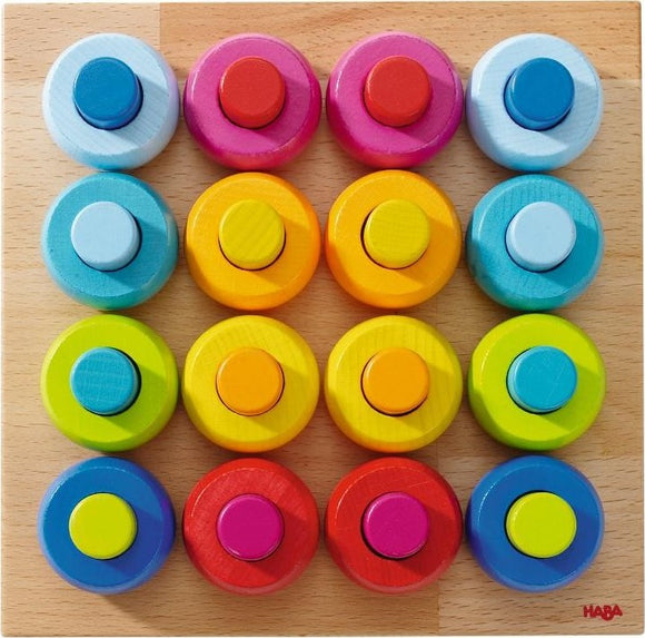 The Pegging Game Rainbow Whirls by Haba features a colorful array of 16 circular pegs in various bright colors, arranged on a light wooden board. Each peg has a unique hue, including blue, pink, yellow, and green, encouraging sensory play and color recognition for children. The design promotes fine motor skills and creative play.