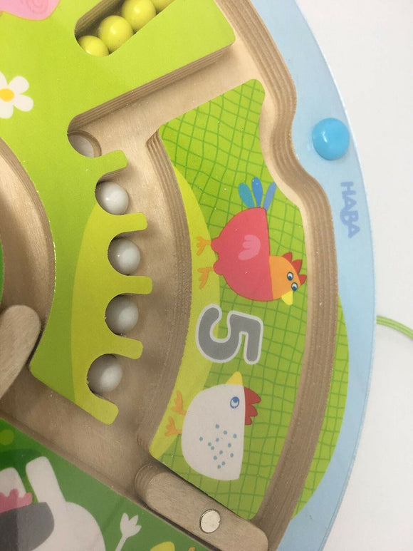 The Magnetic Game Number Maze by HABA features colorful animals and numbers. It showcases a wooden base with vibrant elements including a red bird, a white chicken, and various beads that can move through the maze, promoting early learning and motor skills for young children.
