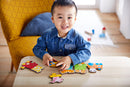 A cheerful young child focuses on assembling a colorful jigsaw puzzle featuring a number train, with various animal-shaped pieces displayed on a wooden table. The child is dressed in a denim shirt and is sitting in a bright room, suggesting an engaging playtime experience.