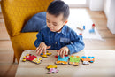 A young child wearing a denim shirt is focused on assembling colorful jigsaw pieces on a wooden table. The vibrant puzzle features animal motifs and numbers, promoting early learning and fine motor skills. The cozy setting includes a yellow patterned chair in the background.