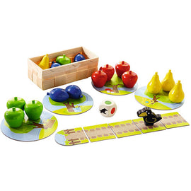 A colorful children's game titled 'My First Orchard' by HABA USA. The game features vibrant wooden fruits including apples, pears, and a basket, along with a die and playing boards depicting trees and paths. The design promotes cooperative play as players work together to collect fruits before the raven reaches the orchard.