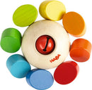 The Clutching Toy Whirlygig by Haba features a central wooden sphere with a red ring and several colorful wooden discs arranged around it. The discs are in varying shades of green, blue, yellow, orange, and red, providing a visually appealing and tactile experience for children. This engaging toy is designed for infants and young children to stimulate sensory exploration and develop fine motor skills.