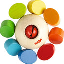 Haba Clutching Toy Whirlygig, featuring a circular wooden base with a red bell at the center surrounded by colorful wooden discs in vibrant yellow, green, blue, orange, and red. Designed for young children, this engaging toy encourages sensory exploration and fine motor skills development.