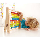 A child interacts with the Hape Rainbow Bead Abacus, a colorful wooden counting toy featuring vibrant beads arranged in rows. The setup encourages learning through play, enhancing fine motor skills and cognitive development.