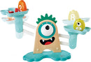 The Monster Math Scale is a colorful educational toy featuring a playful monster design. It has a central wooden base with a large single eye, fanged mouth, and spiky green hair. Two balancing arms extend from the base, each equipped with shallow bowls. In the bowls, there are various colorful items including numbered weights and fruits, encouraging children to engage in hands-on math activities and enhance their counting skills.