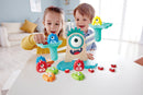 A colorful Monster Math Scale toy by HaPe International, featuring a playful, one-eyed monster figure and various numbered weights in bright colors. Two children, a boy and a girl, are engaged in a learning activity, weighing the colorful pieces on the scale while smiling, enhancing their math skills through play.