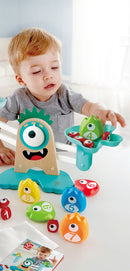 A young child engages with the HaPe International Monster Math Scale, a vibrant educational toy featuring a friendly monster design. The scale includes colorful number tokens in various shapes and sizes, fostering early math skills through interactive play. The setting is bright and cheerful, perfect for imaginative learning.
