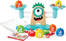 The Monster Math Scale by HaPe International features a playful, monster-themed scale with colorful counting pieces including numbers 1 to 10. It has two weighing buckets, each designed to hold vibrant counting tokens shaped like flame characters in various colors, facilitating engaging fun while learning basic math concepts. The set comes with a storage bag and an instructional booklet illustrating games and activities.