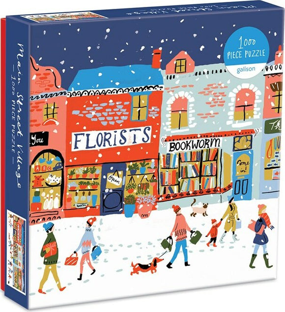 Main Street Village jigsaw puzzle by Galison featuring a whimsical winter scene with a street lined with colorful shops, including a florist and a bookstore. People are seen walking with shopping bags, with dogs in tow, all against a snowy backdrop.