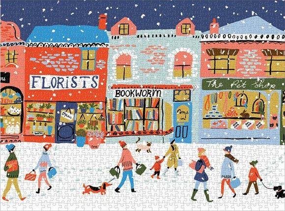 A colorful jigsaw puzzle depicting a charming village street scene in winter. The image features shops like a florist, a bookstore named 'Bookworm,' and 'The Pet Shop.' People, including children and pets, stroll along the snowy street, carrying shopping bags. The vibrant artwork showcases various building styles in a festive atmosphere.