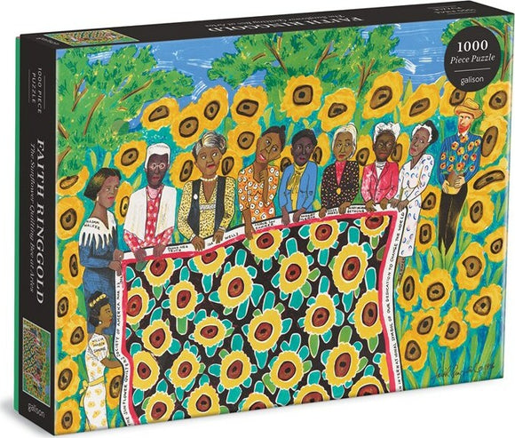 The Sunflower Quilting Bee at Arles jigsaw puzzle by Galison features a vibrant illustration of diverse figures gathering around a quilt with sunflowers, set against a colorful background of greenery and blue sky. The puzzle comes in a sleek black box showcasing the artwork.