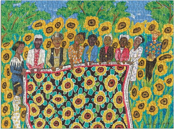 A vibrant jigsaw puzzle featuring a colorful illustration of several figures surrounded by sunflowers. The scene depicts a group of women holding a large quilt adorned with sunflowers, set against a backdrop of lush greenery and a blue sky.