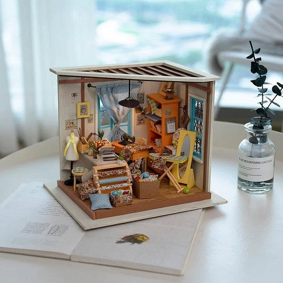 A detailed DIY model kit of Lisa's Tailor, showcasing a miniature tailor workshop with colorful furniture, a sewing machine, and decorative items. The scene is cozy, with a window, bookshelves, and various crafting supplies, displayed in an open box design on a light surface.