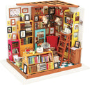 A detailed and vibrant miniature model of a study room, featuring colorful bookshelves filled with various books, a stylish red chair, and decorative items like framed pictures and potted plants. The model also showcases a wooden ladder and a table stacked with books, creating a cozy reading environment.